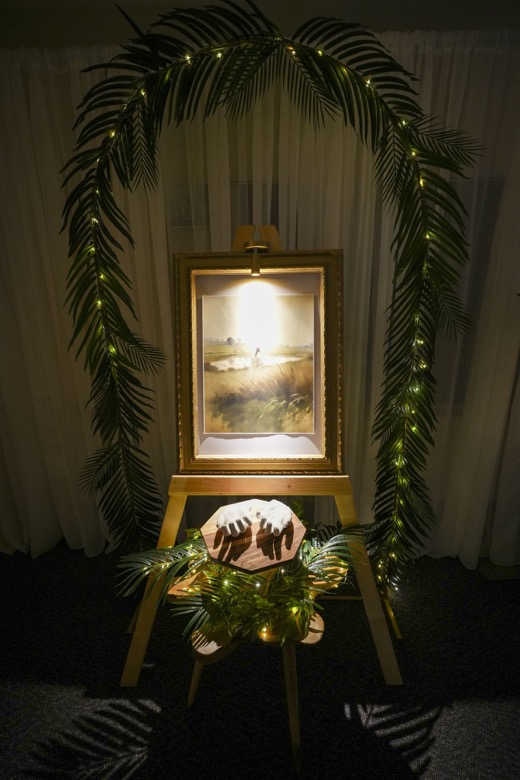 An arch of palm leaves and small lights around a glowing painting of Christ.